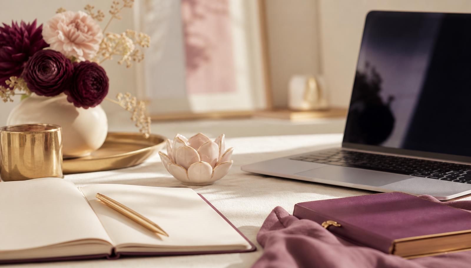 Elegant workspace with laptop, journal, gold pen, plum flowers, and a ceramic lotus — representing branding from the inside out